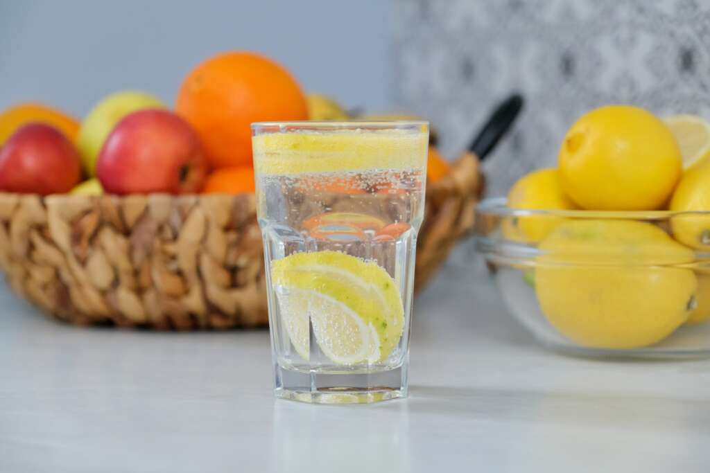 Glass of lemon water with fresh fruits, symbolizing natural detox and hydration